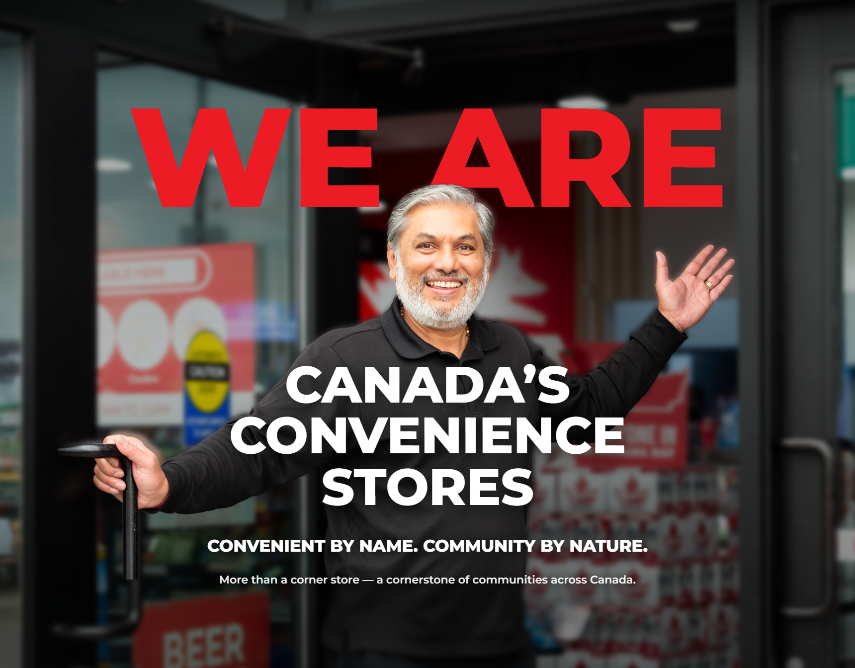 A convenience store owner smiling and welcoming customers from his shop's doorway